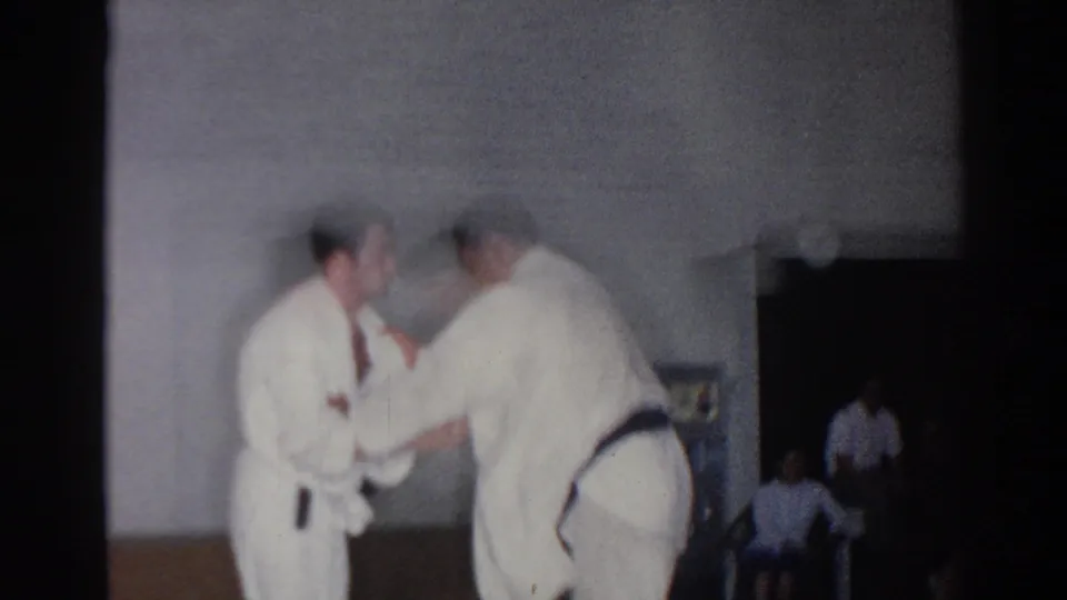 In San Gabriel, California in 1966, two men in white judo gis practice a close-contact technique in a gymnasium.