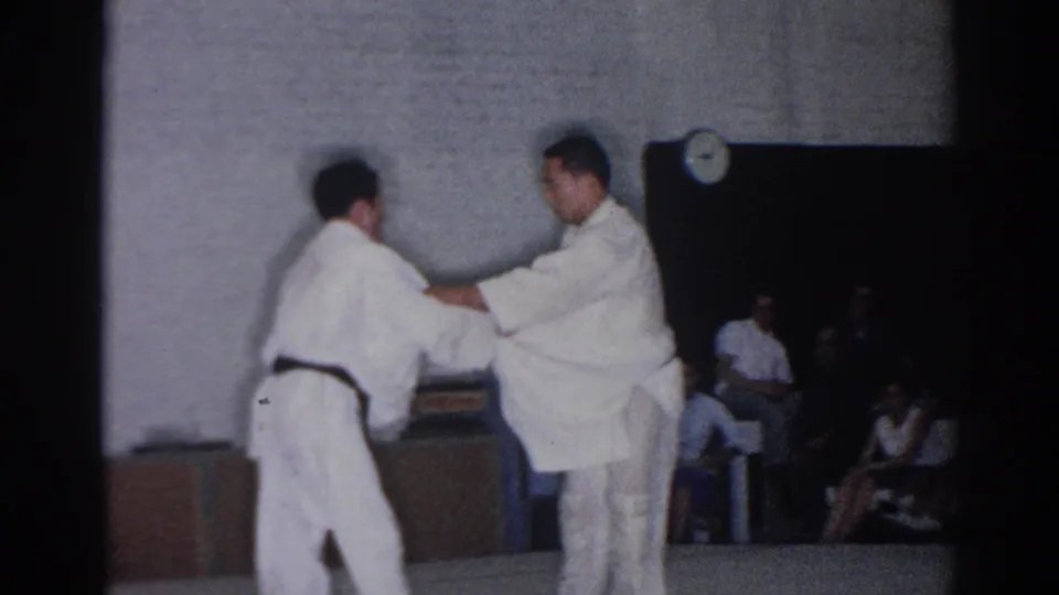 The two black-belt competitors reset their grips on the gym floor during the 1966 San Gabriel karate tournament footage.