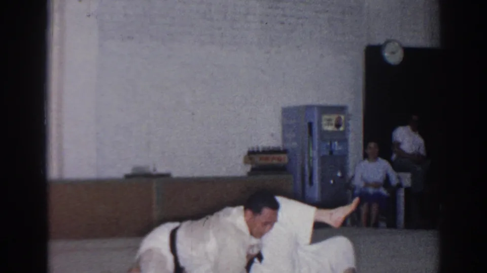 Near the end of the San Gabriel tournament clip, one karate fighter stays low on the mat while the other is partly visible beside him.