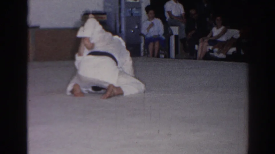 In the final frame, two martial artists in white gi remain on the mat during the 1966 San Gabriel demonstration, with spectators visible behind them.
