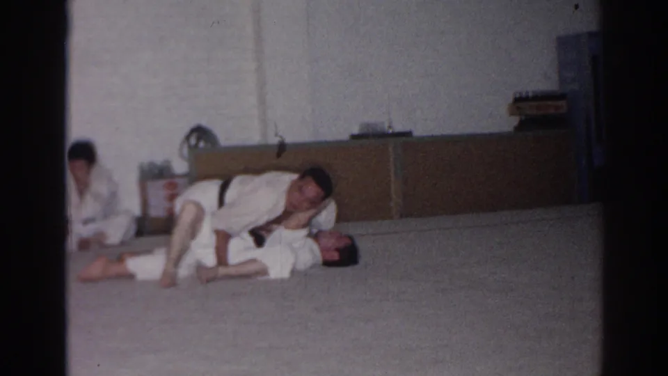 1966 San Gabriel frame of a gi-clad practitioner controlling a partner on the floor during indoor martial arts practice.