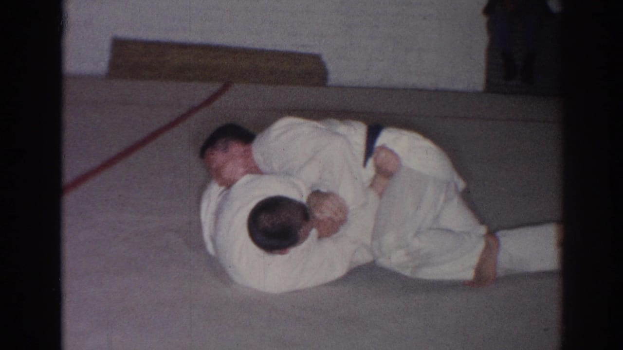 Two judo practitioners in white uniforms grapple near a red line on the mat.
