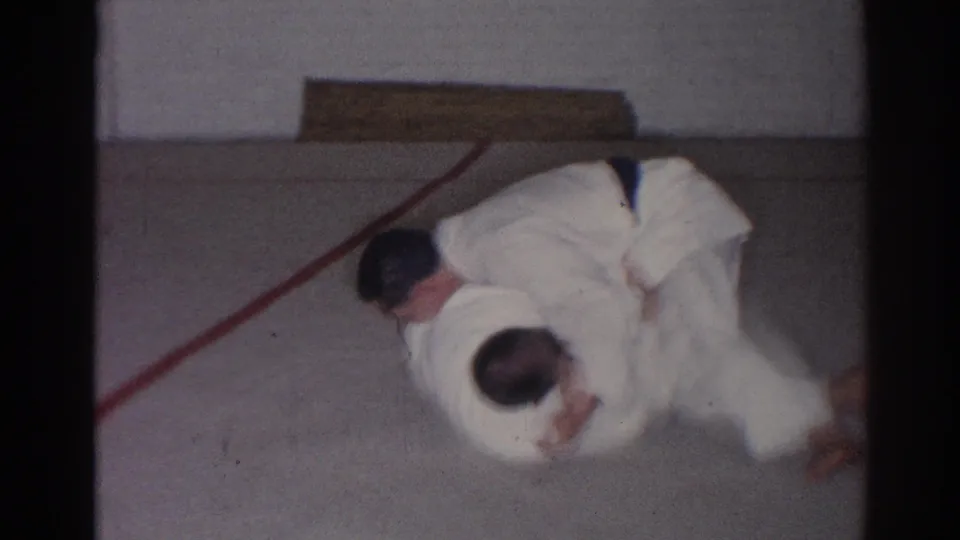 1966 San Gabriel home-movie frame showing a close ground-grappling moment between two judoka on an indoor mat.