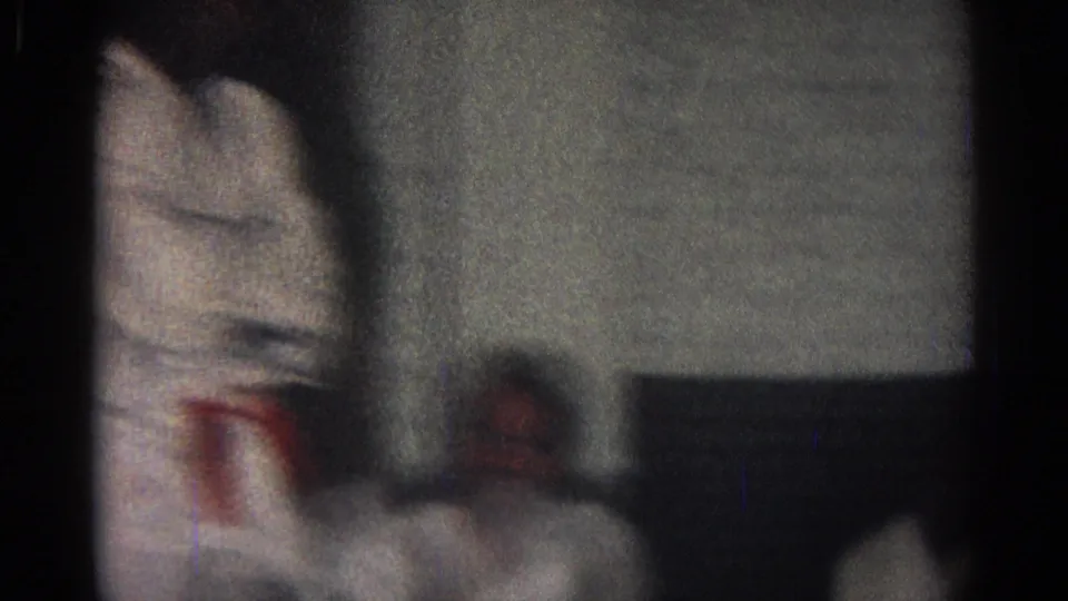 A soft, close 8mm view shows part of a white gi with a red belt, with a seated figure blurred in the background.