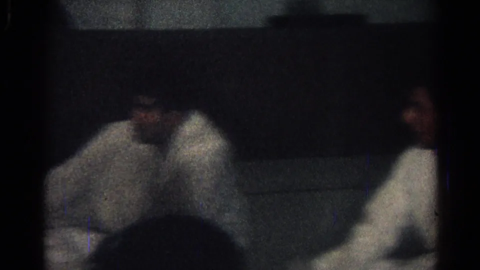 Several men in white gi sit or kneel inside the dim San Gabriel dojo, with dark film edges and heavy grain visible.