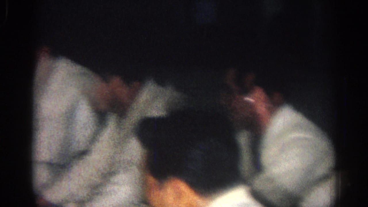 Judo athletes in white uniforms gathered in a dim indoor room.