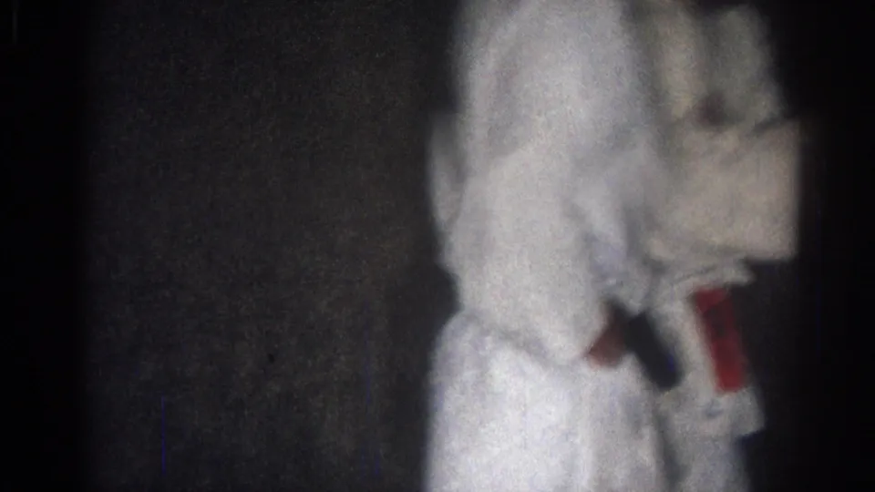 1966 San Gabriel frame showing a judo athlete in a white gi standing at the edge of a dim indoor training space.