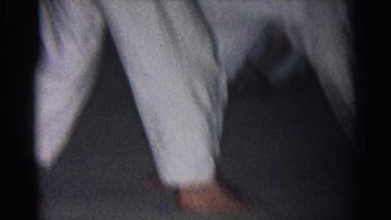 Close view of white uniformed legs and bare feet moving across a dark floor.
