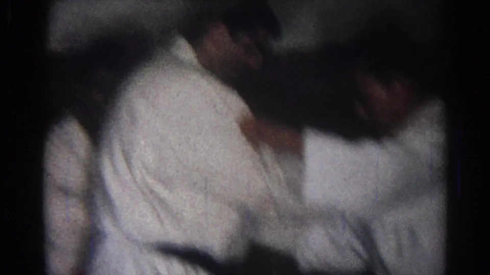 Blurred 1966 San Gabriel frame of two adult men in white martial arts uniforms practicing a hold or takedown indoors.