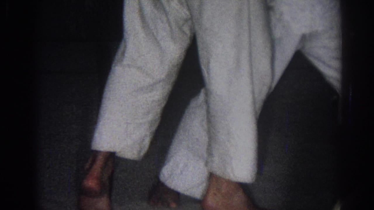 Two practitioners in white gi uniforms move in close contact in a dim room.