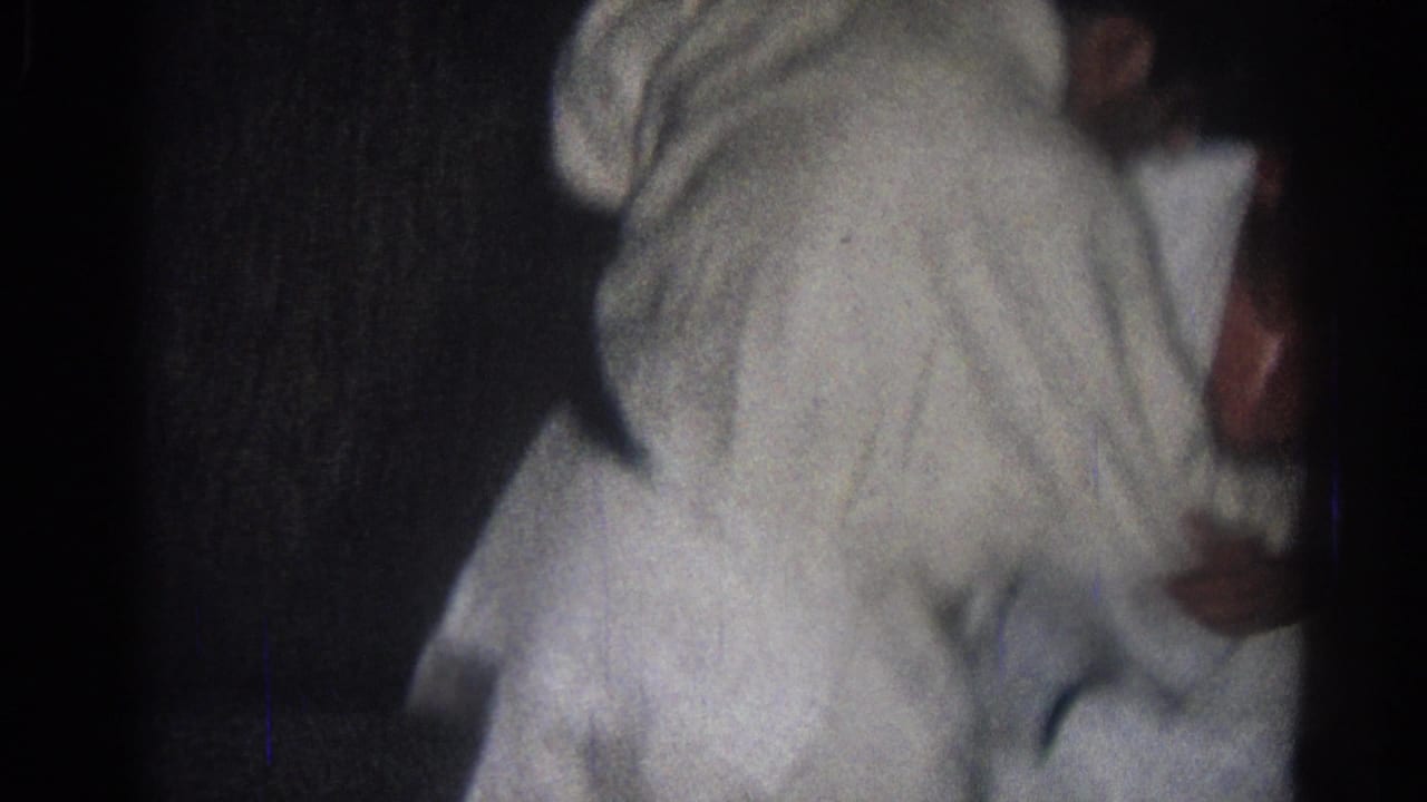 Two adults in white gi practice close-contact martial arts on a dark indoor mat.