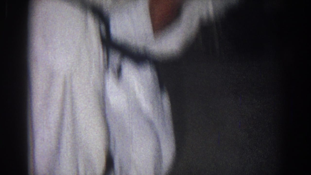 A close, soft-focus view shows a gi-clad martial artist shifting position in the dim San Gabriel practice setting.