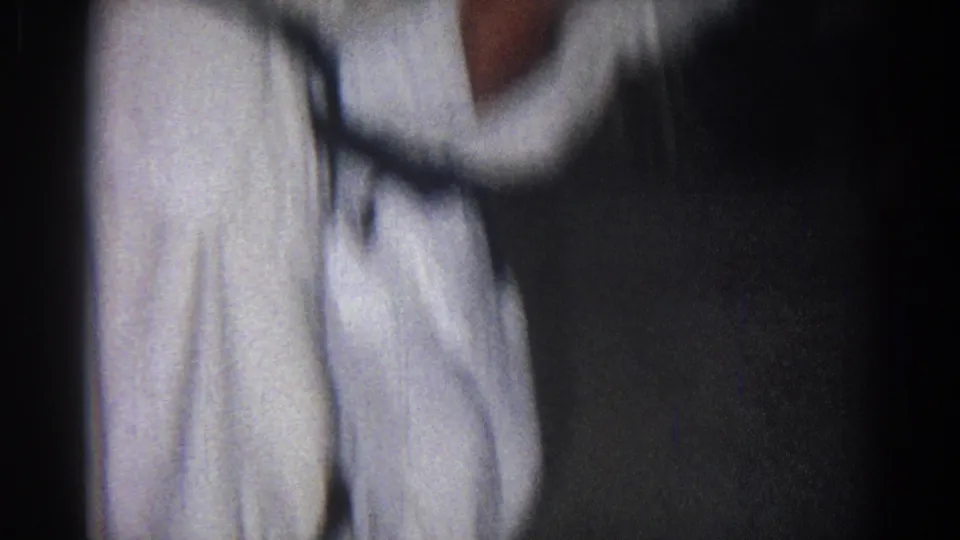 A close, soft-focus view shows a gi-clad martial artist shifting position in the dim San Gabriel practice setting.