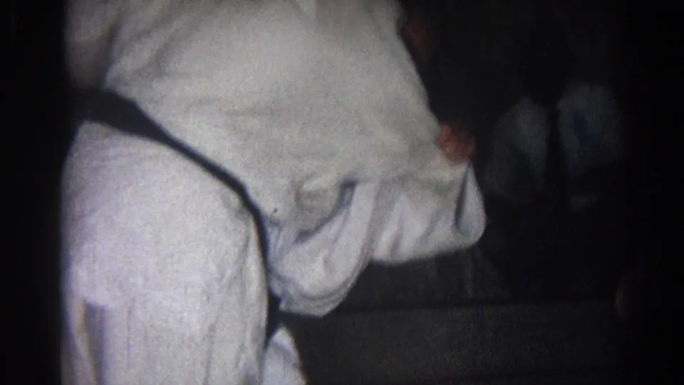 Two adults in white gi crouch close to the mat, appearing to work through a hold or throw in the 1966 San Gabriel clip.