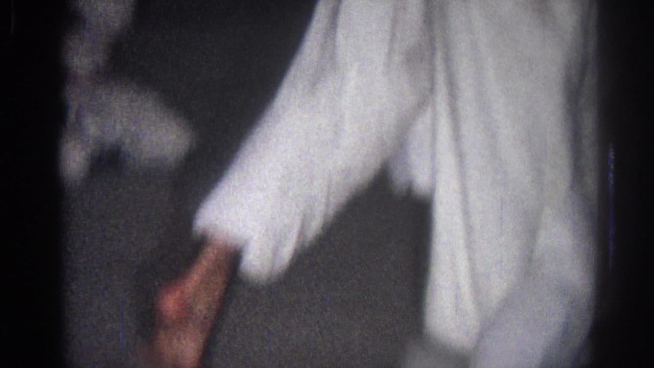 In 1966 San Gabriel home-movie footage, a practitioner in a white gi is cropped at the torso and legs during indoor movement.