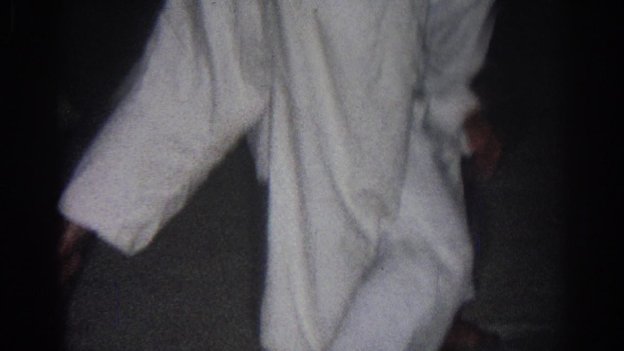 Cropped view of a white-uniformed practitioner with a bare hand and dark floor behind them.
