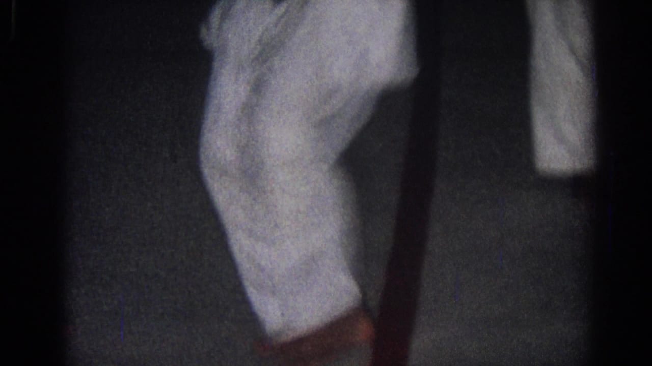 Two people in white gi stand close together in a dark indoor room.