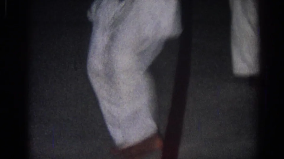 1966 San Gabriel home-movie frame showing two judo practitioners in white gi beginning a close grappling position indoors.