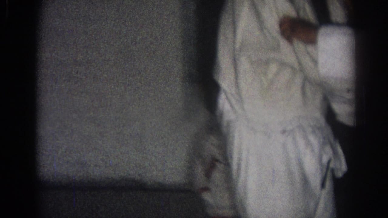 A person in a white gi is partly visible beside a dark wall or mat.