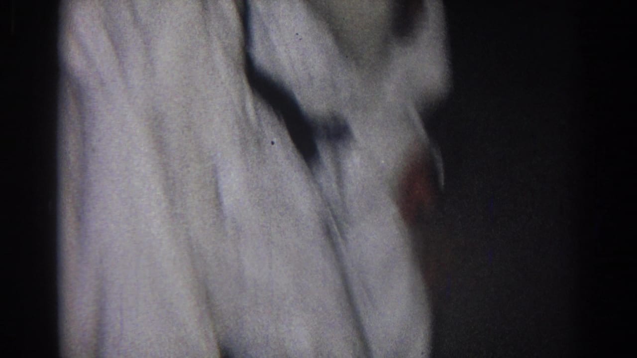 Close view of two people in white martial arts uniforms grappling in a dark indoor space.