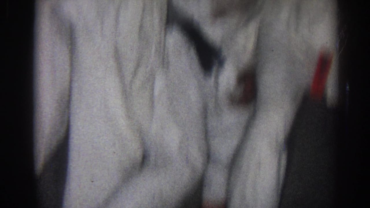 1966 San Gabriel home-movie frame showing partial views of karate students in white gi and dark belts during close practice.