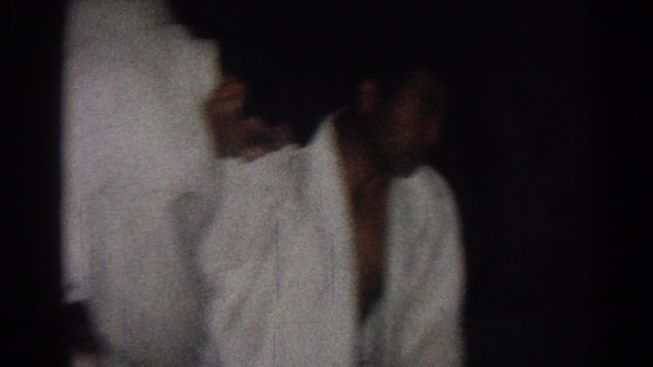 A karate student in a white gi appears in profile during practice, filmed in low light in San Gabriel, California, 1966.