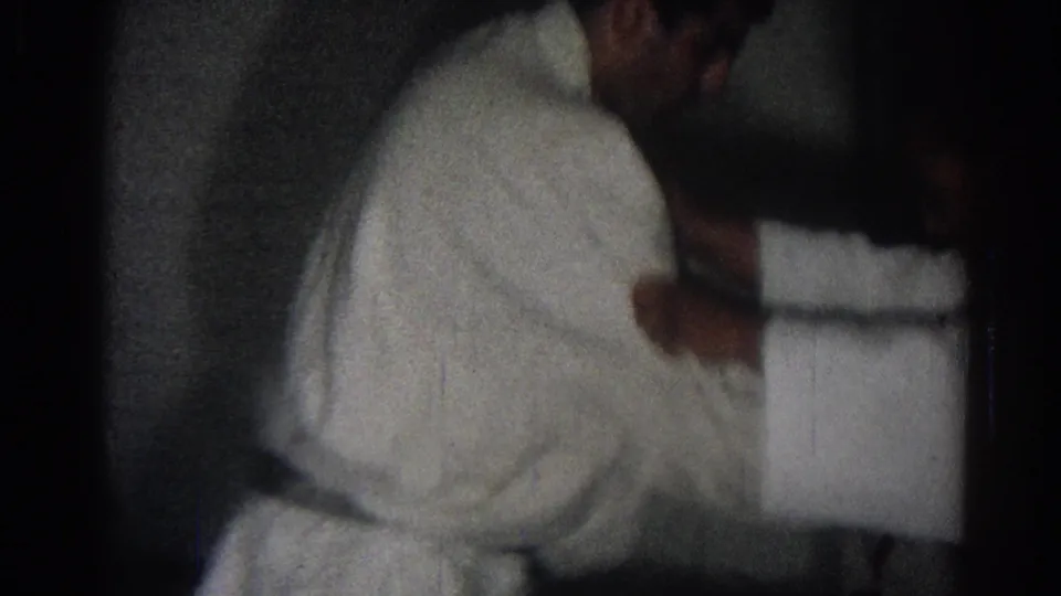 Two students in white karate uniforms appear to practice a close-range technique in dim 1966 San Gabriel home-movie footage.