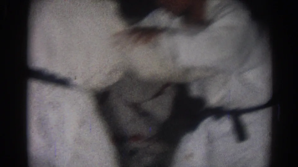 Students in white gi and dark belts lean into a paired karate drill, captured with motion blur and grain on 8mm film.