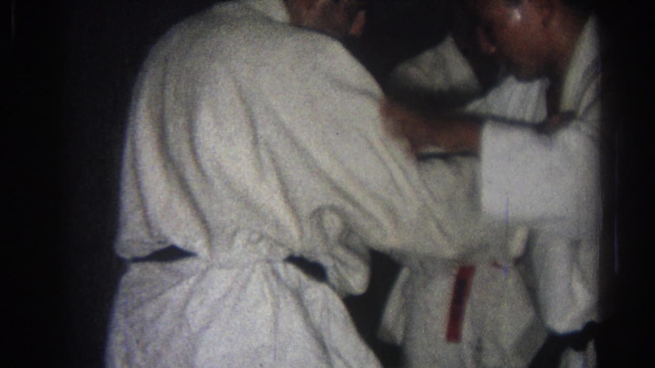 Two adult men in white gi appear to practice a close-contact karate or martial arts technique indoors in 1966 San Gabriel footage.