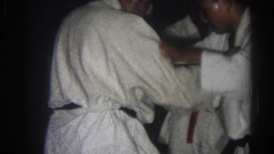Two adult men in white gi appear to practice a close-contact karate or martial arts technique indoors in 1966 San Gabriel footage.