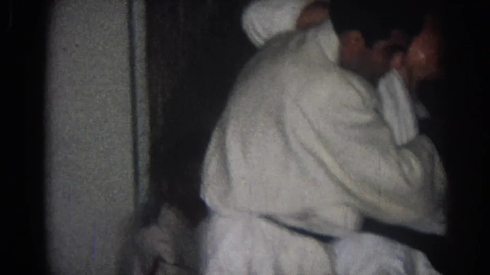 Adult men in white gi practice a controlled throwing movement in a dim indoor San Gabriel martial arts scene from 1966.