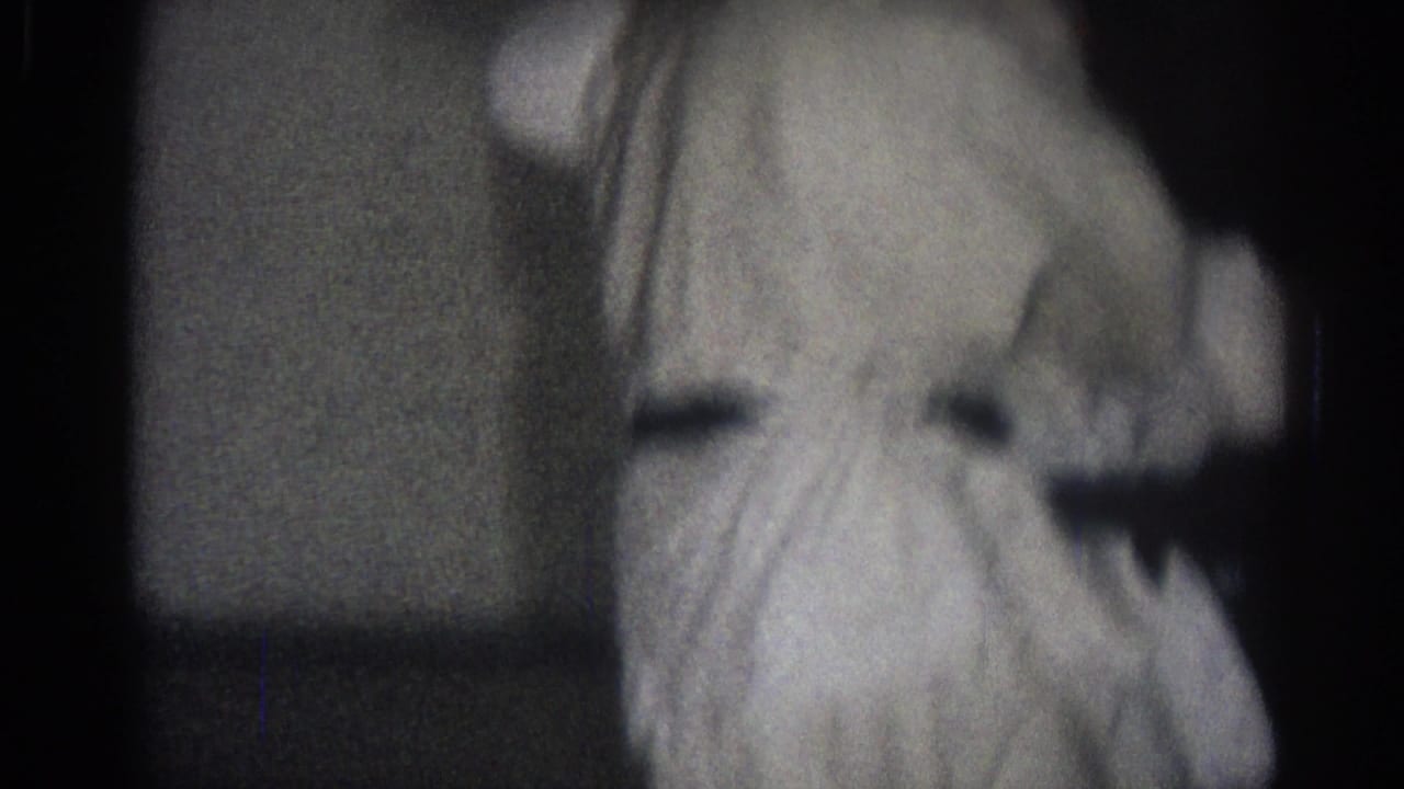 Two people in white martial arts uniforms moving in a dark indoor space.