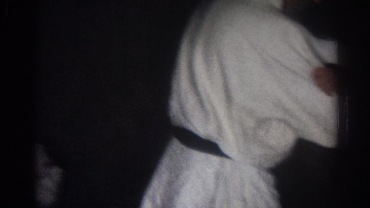Man in a white martial arts uniform turned sideways in low light.
