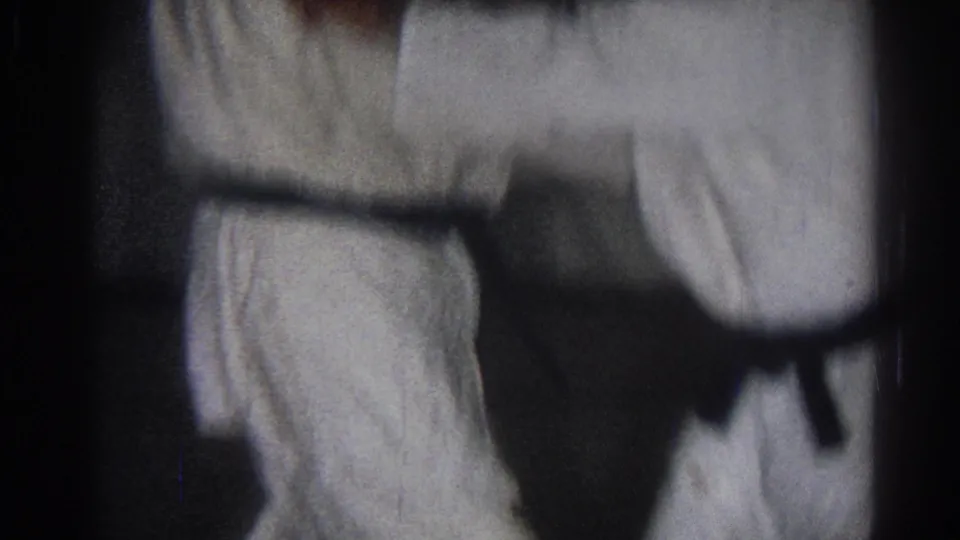 Close 8mm frame of two white-uniformed practitioners with arms crossing during karate practice in San Gabriel, California.
