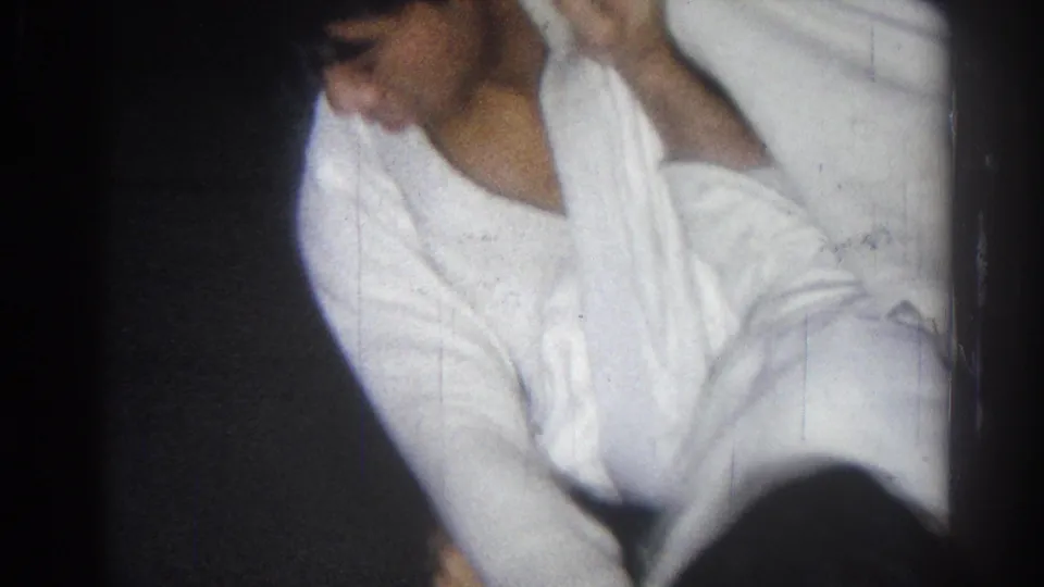 Two men in white karate uniforms practice close together, with one partly visible face in the dim 1966 San Gabriel footage.