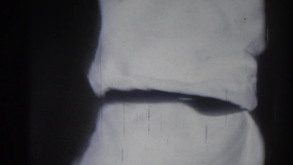 1966 San Gabriel home-movie frame showing two martial arts practitioners in white uniforms, partly cropped and softly focused.