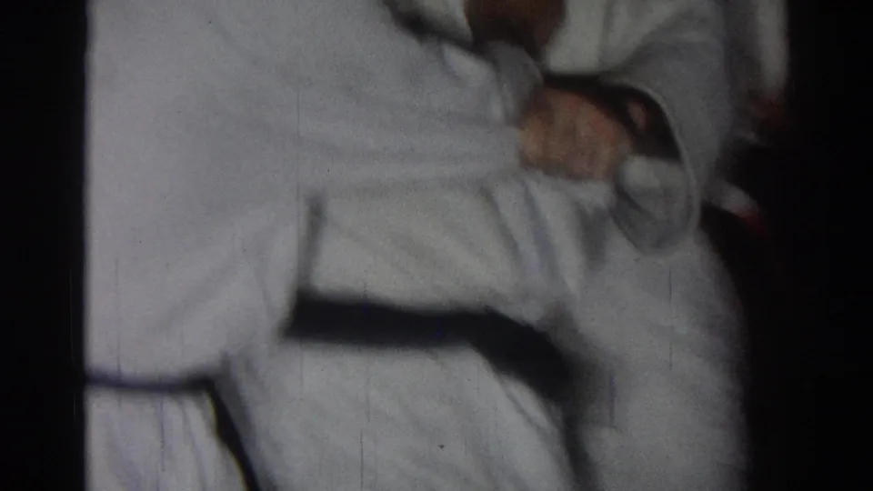 1966 San Gabriel frame showing a white-uniformed martial arts practitioner bracing low during a judo-style demonstration.