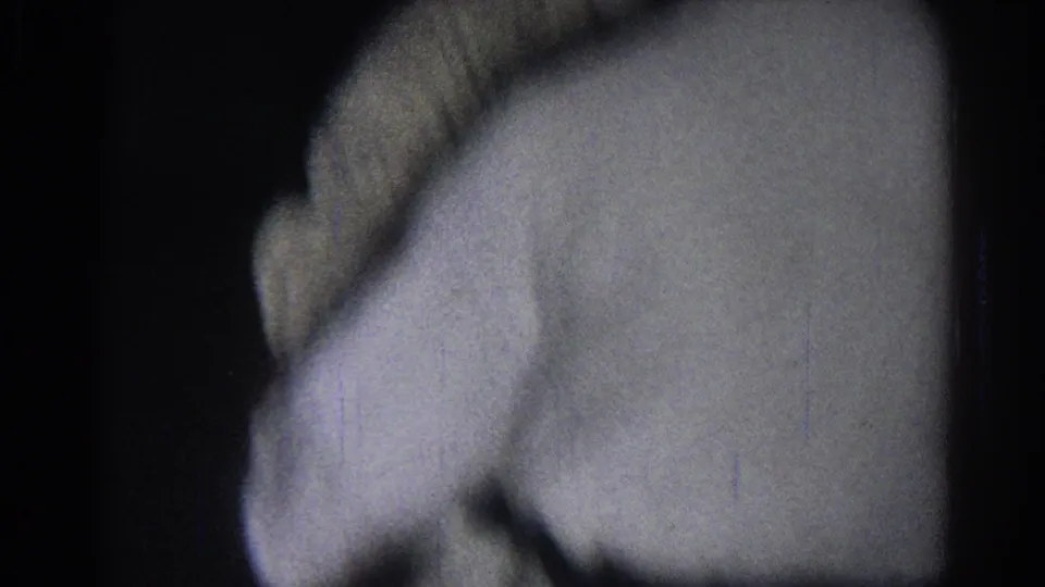 San Gabriel 1966 frame showing a close side view of a white-robed practitioner moving through a dark indoor space.