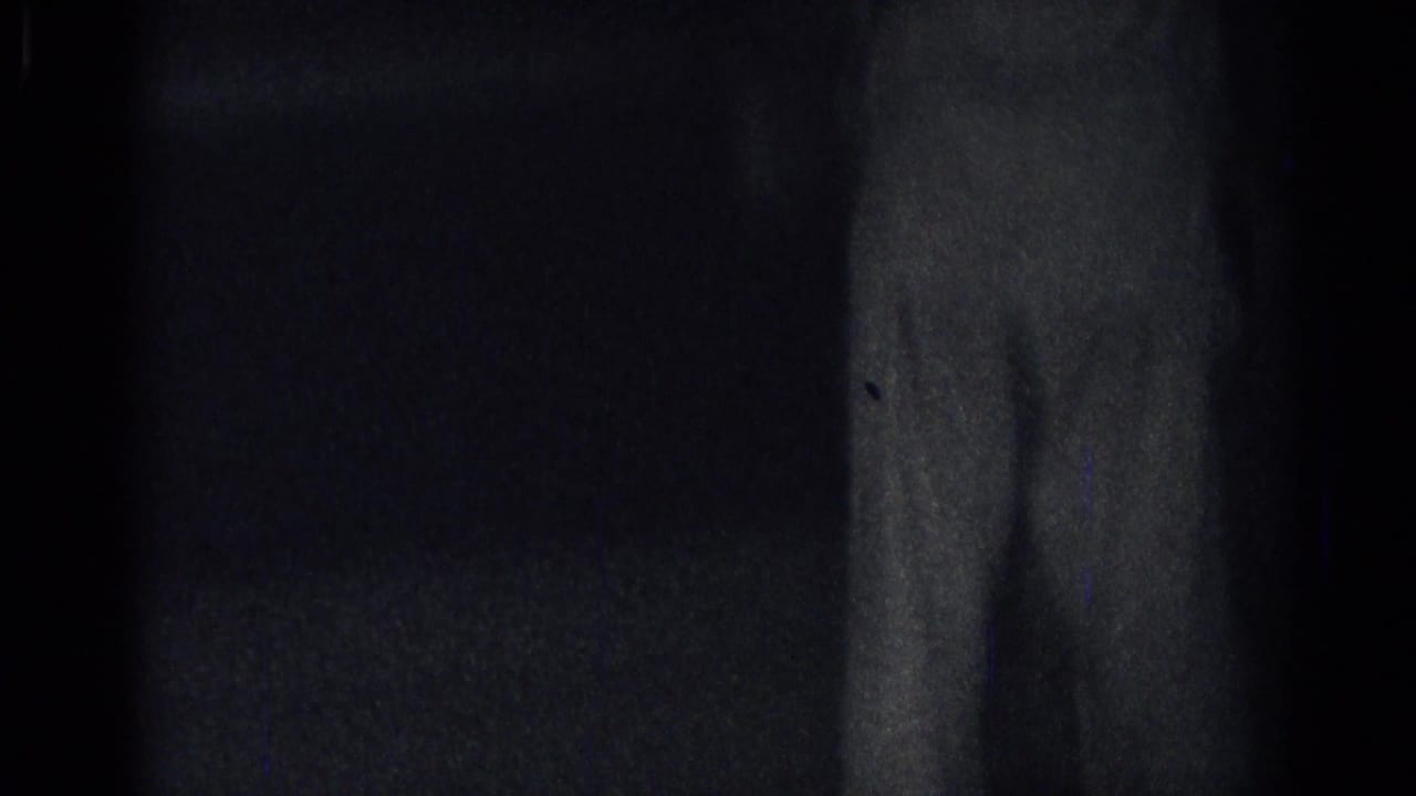 Mostly dark frame with a faint wall or doorway edge at right.