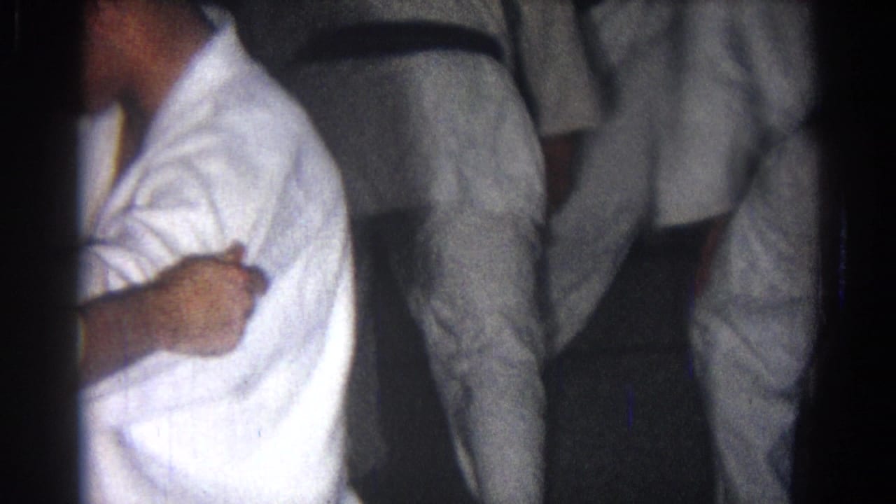 Practitioners in white gi uniforms and black belts stand close together in a dark training space.