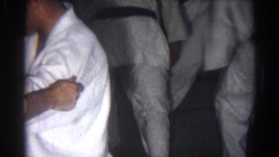 1966 San Gabriel home-movie frame showing cropped martial arts practitioners in white gi uniforms and black belts during class.