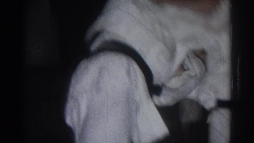 1966 San Gabriel home-movie frame showing a white-gi practitioner bent forward during sparring with another figure partly visible.