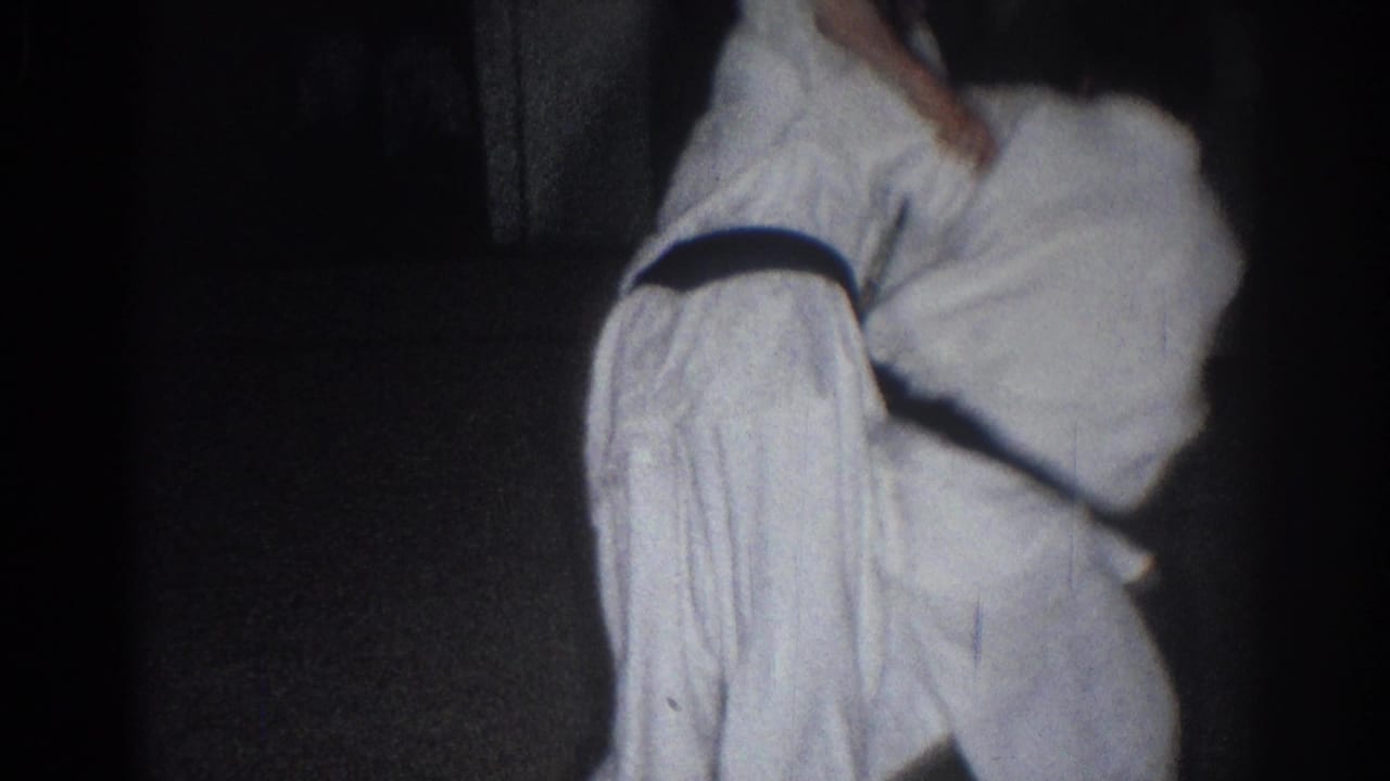 In 1966 San Gabriel home-movie footage, two boys in white martial arts uniforms and dark belts practice a close grappling hold indoors.