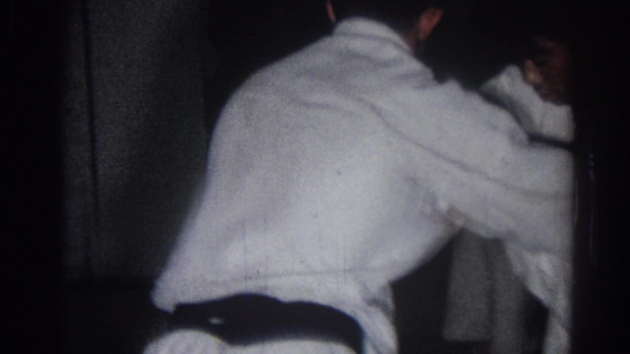 A handheld 1966 San Gabriel frame shows a boy in a white gi and dark belt leaning into a martial arts movement with another student partly visible.