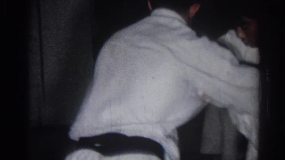A handheld 1966 San Gabriel frame shows a boy in a white gi and dark belt leaning into a martial arts movement with another student partly visible.