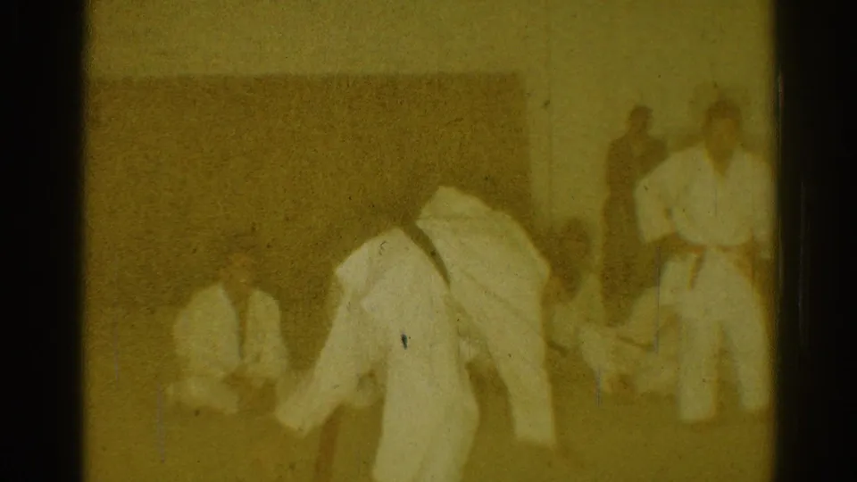 A yellow-tinted 8mm frame shows a karate practice moment with white uniforms, dark belts, and observers along the edge of the mat.