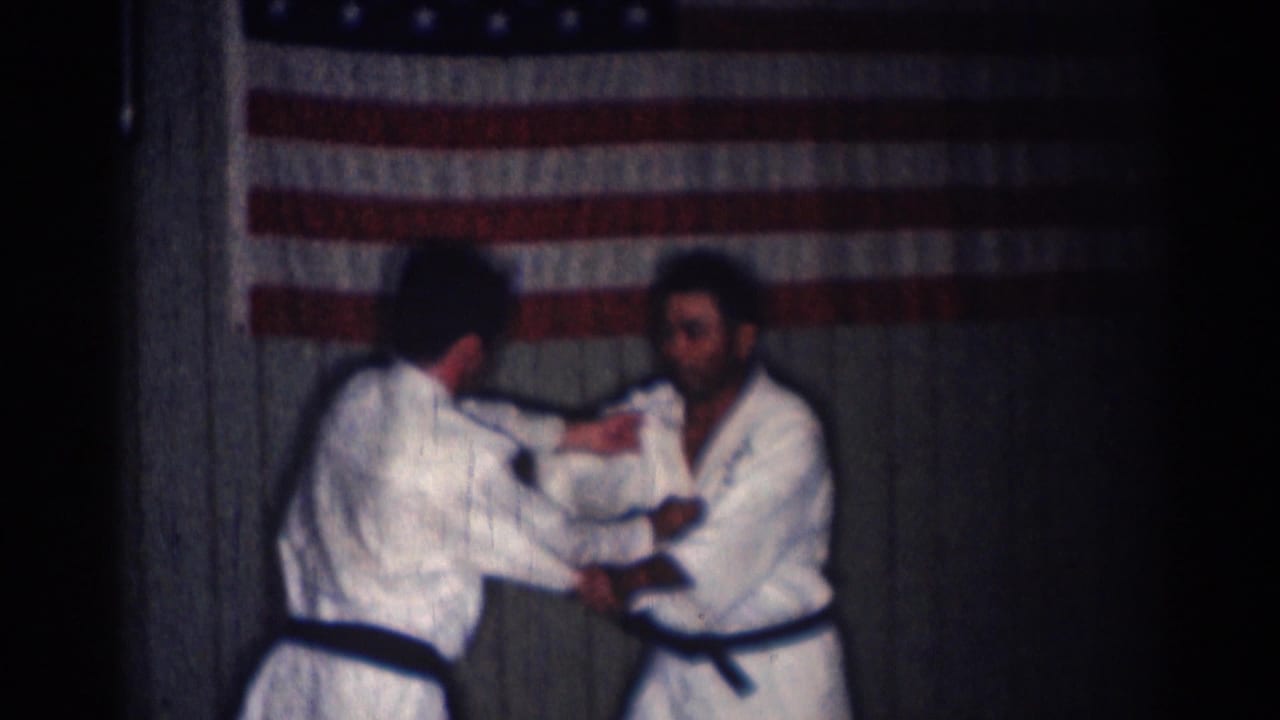 In 1966 San Gabriel footage, two men in white martial arts uniforms practice a close-contact technique before an American flag.