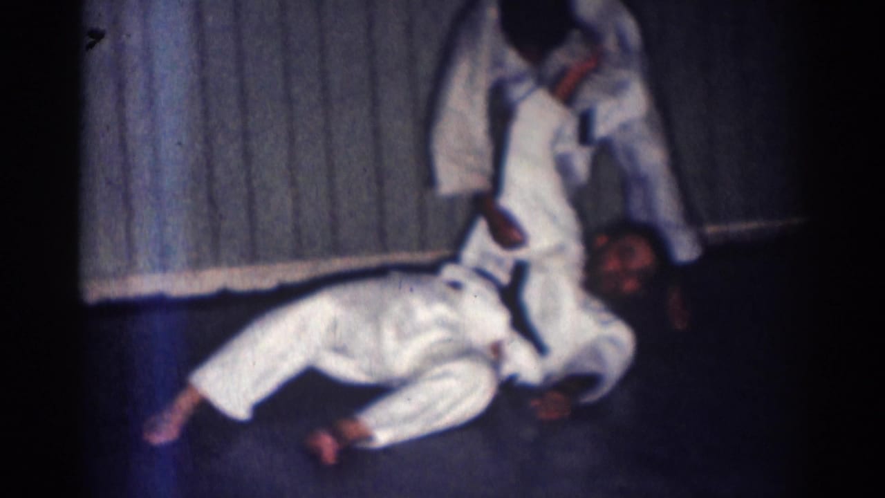 A black-belt practitioner completes a controlled throw as his training partner lands on the mat inside the San Gabriel dojo setting.
