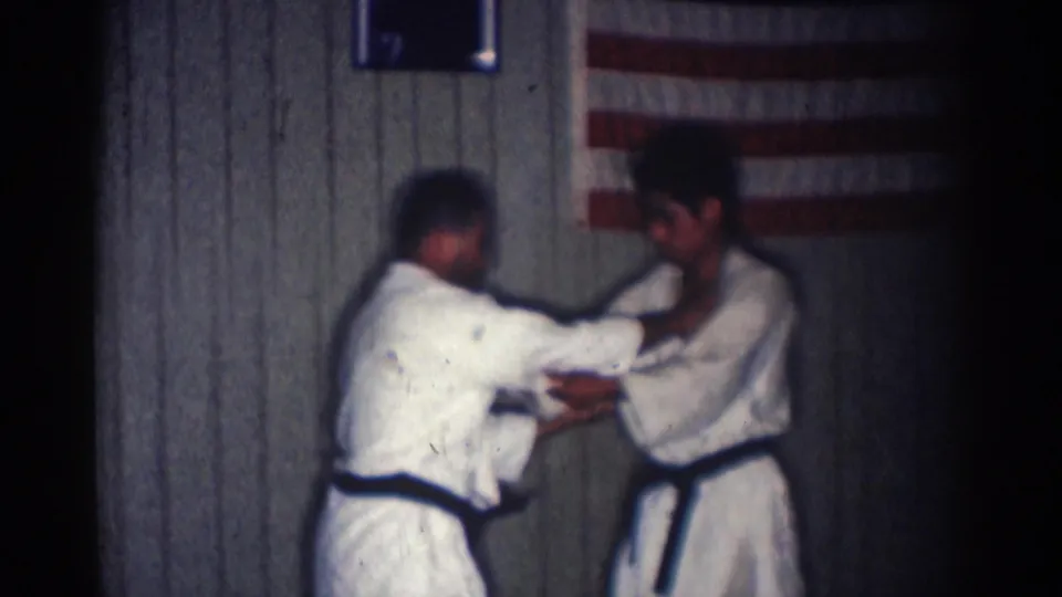 The training partners grip each other at close range while practicing a standing technique in the 1966 San Gabriel dojo interior.
