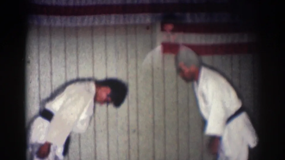 Two adult martial artists reset after a technique, with one bending forward and the other standing on the gym mat in San Gabriel.